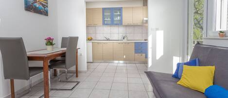 Una cocina moderna con armarios azules, una zona de comedor con una mesa y sillas de madera, y un sofá gris con cojines coloridos.