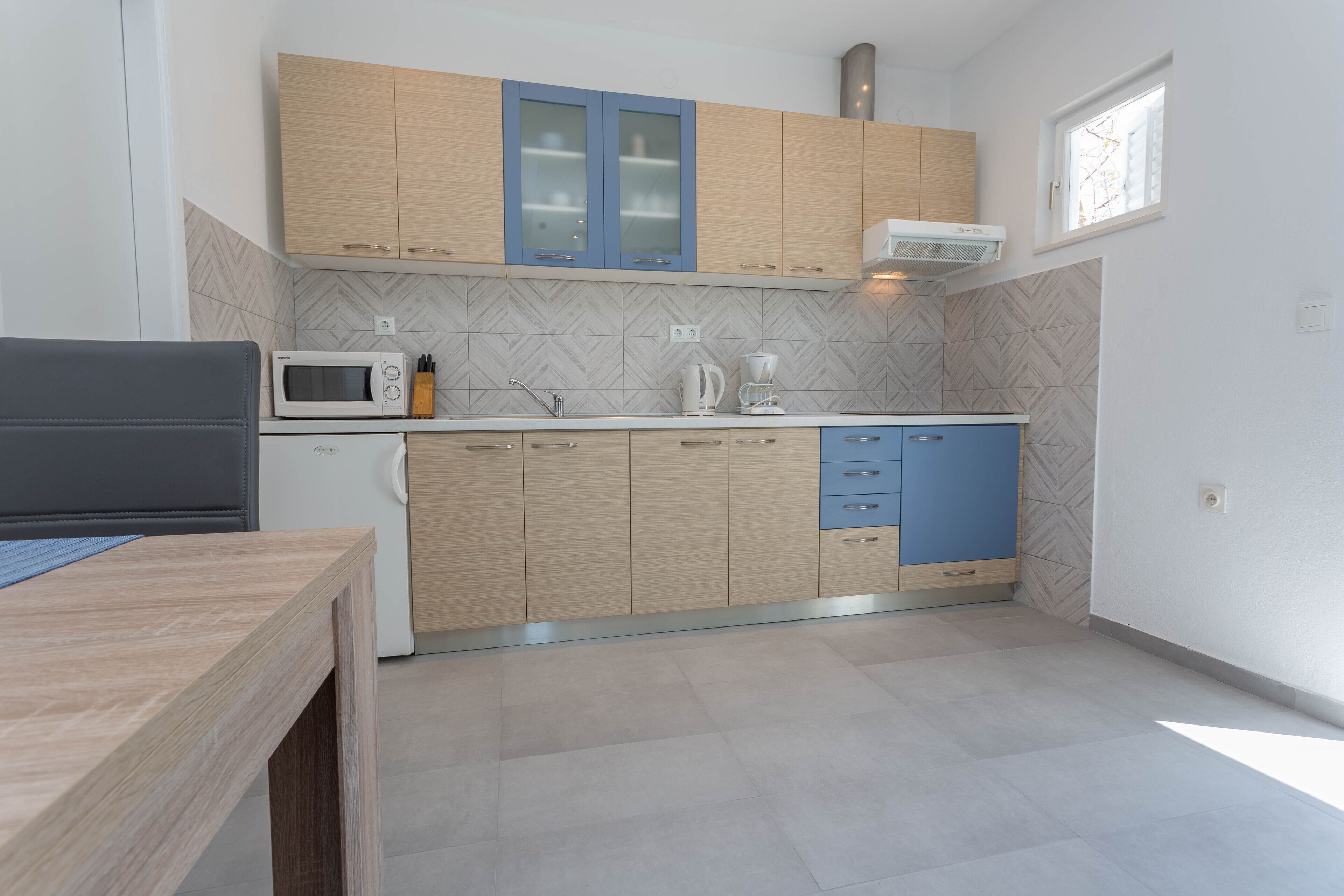 A modern kitchen with light wood cabinets, a microwave, a coffee maker, and a window providing natural light.