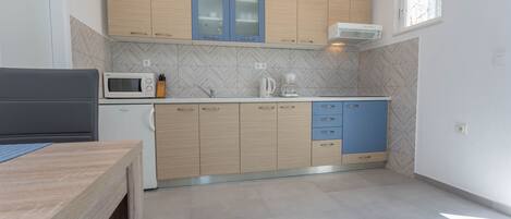 A modern kitchen with light wood cabinets, a microwave, a coffee maker, and a window providing natural light.