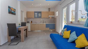 A compact living space with a kitchenette, a dining area, and a sofa with cushions. - Apartmani Ivanovic (Hvar)