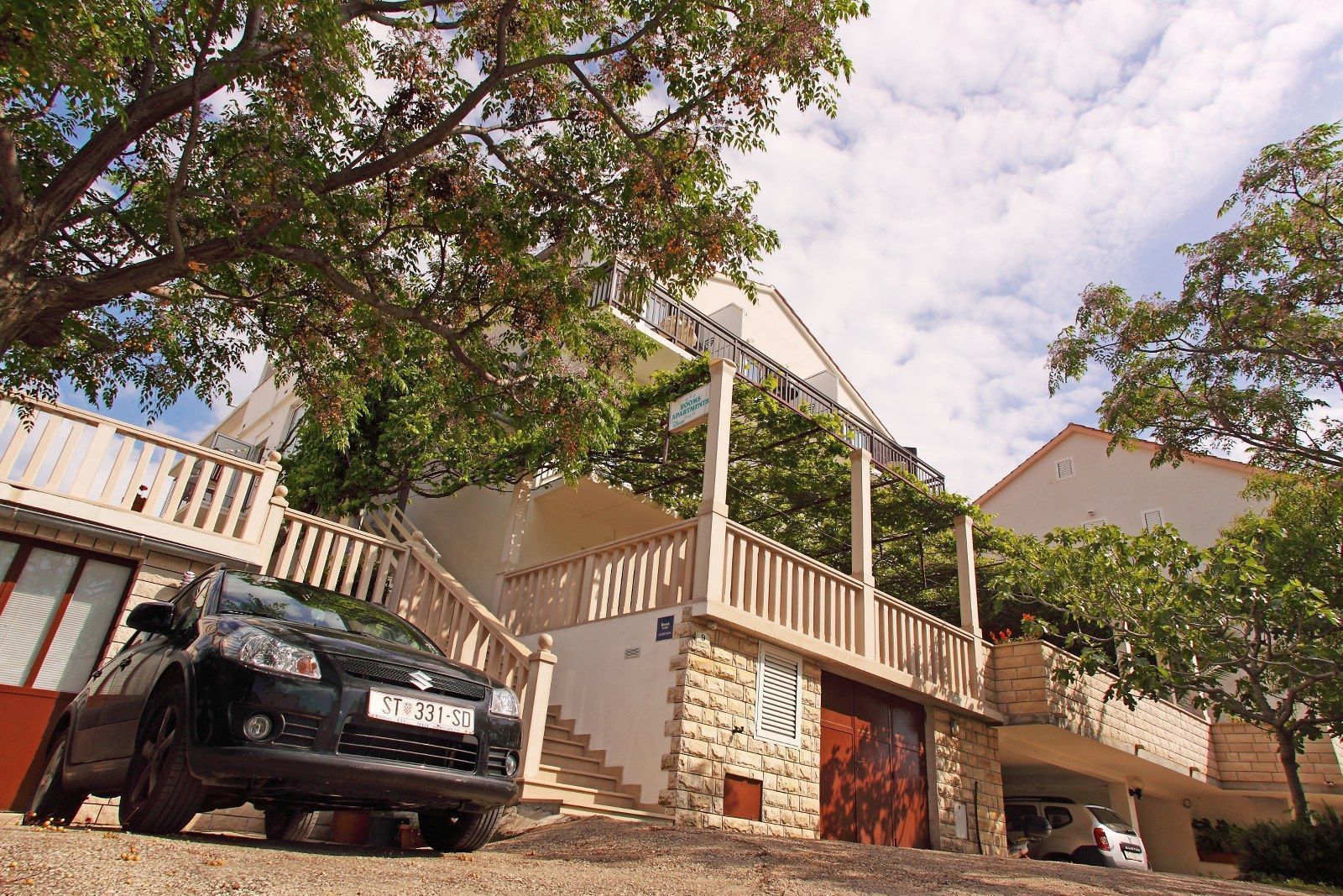 A two-story building with a balcony, a staircase, and a parked car.