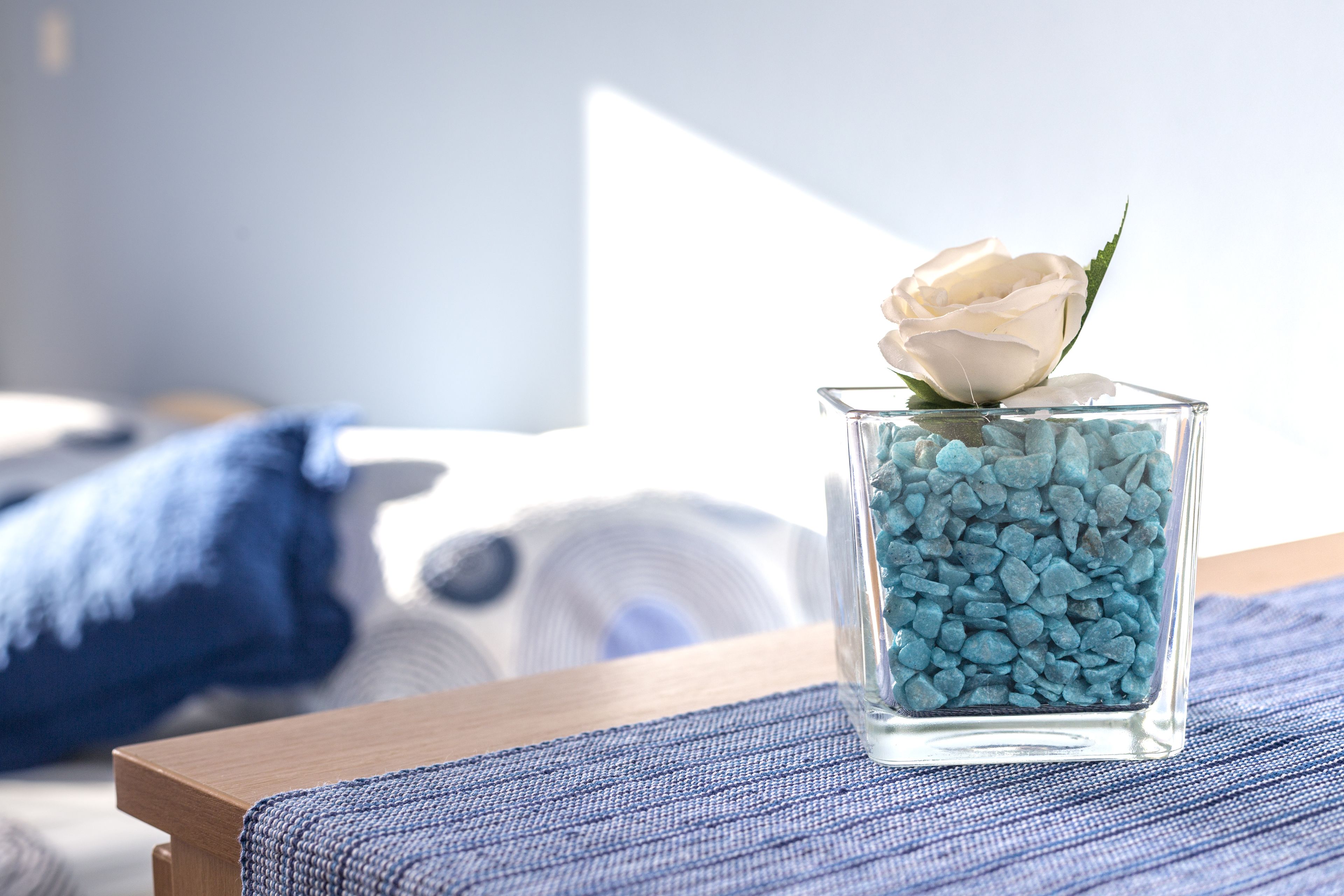A clear glass vase with a white rose on a blue textured surface.