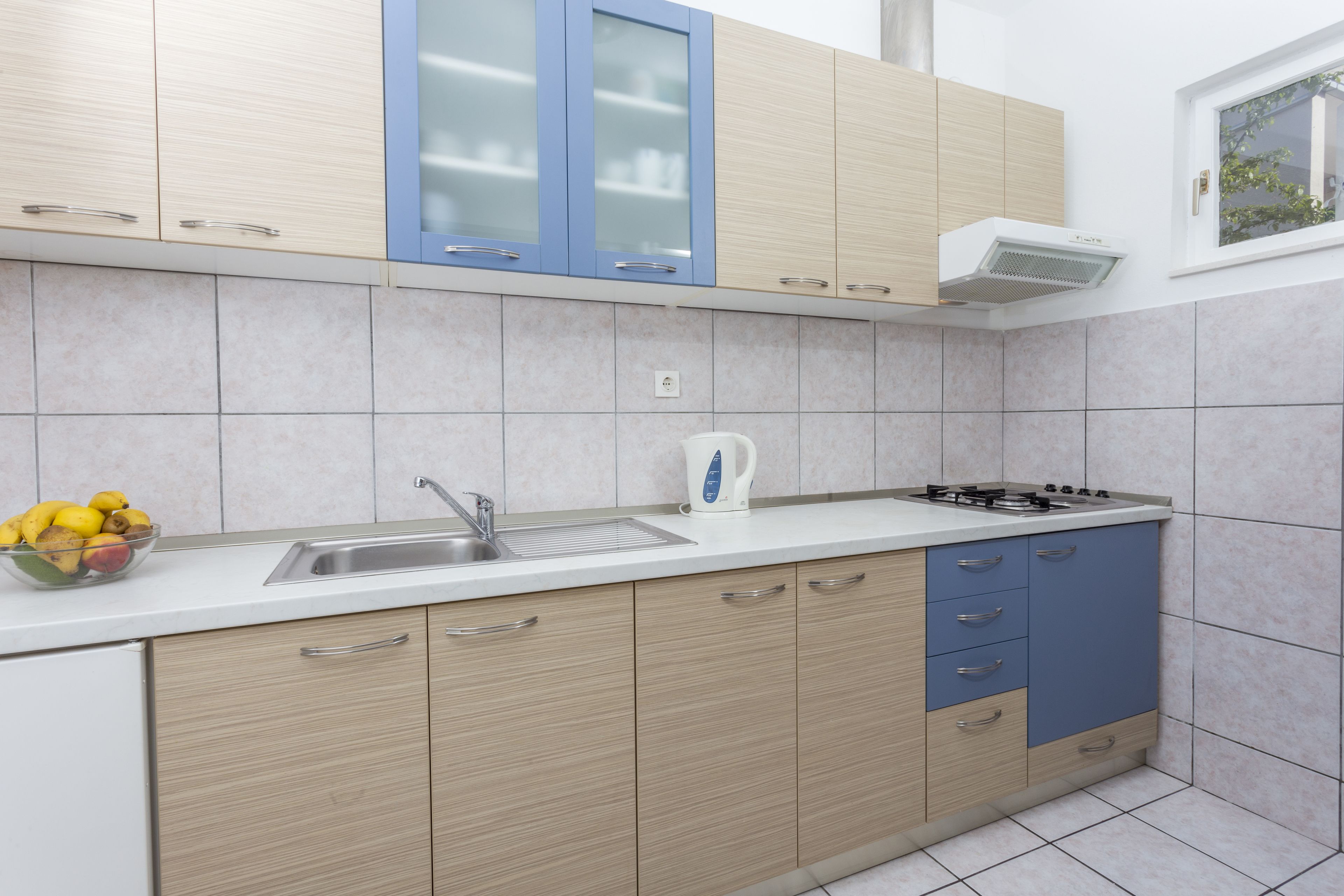 Una cocina moderna con armarios de madera clara, un lavamanos de acero inoxidable y una estufa a gas.