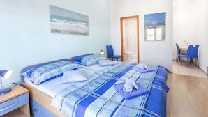 A bedroom with two beds, a desk, and a chair. There are paintings on the walls and an air conditioning unit above the bed. - Apartmani Ivanovic (Hvar)