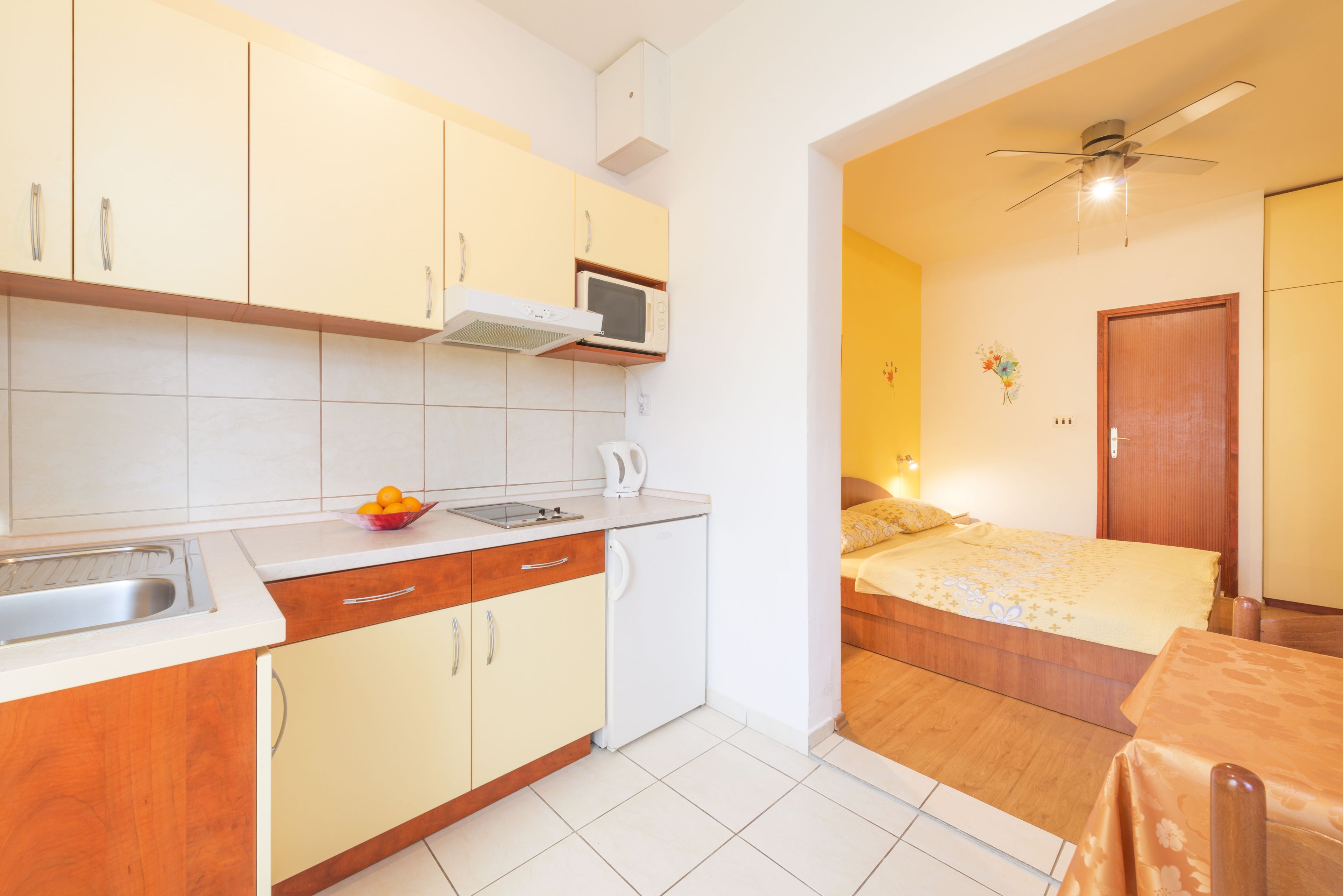 A compact kitchen with a microwave, sink, and a bowl of fruit on the counter.
