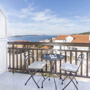 A balcony with two chairs and a small table, overlooking a coastal view with buildings and a clear sky. - Apartmani Ivanovic (Hvar)