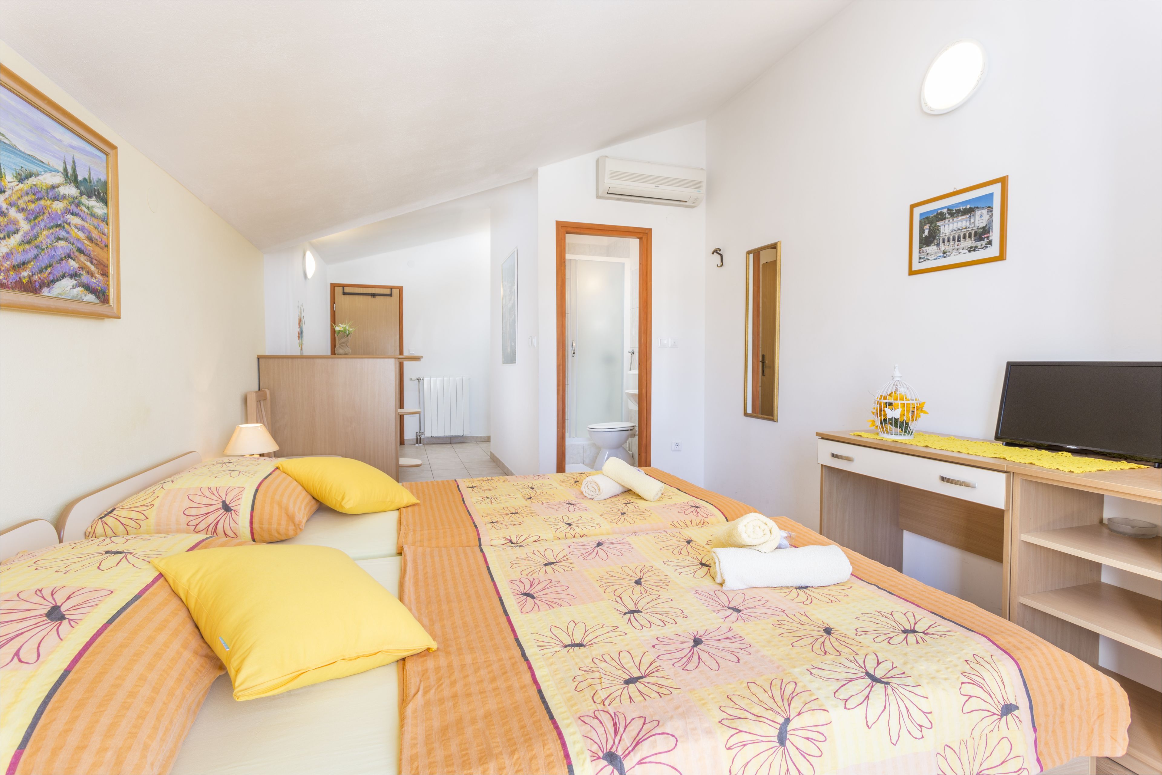 A hotel room with two beds, a desk, a TV, and a bathroom visible in the background.