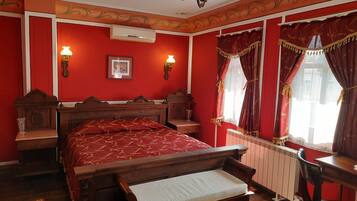 Una habitación tradicional con una cama de madera, un banco, un radiador y una ventana con cortinas.