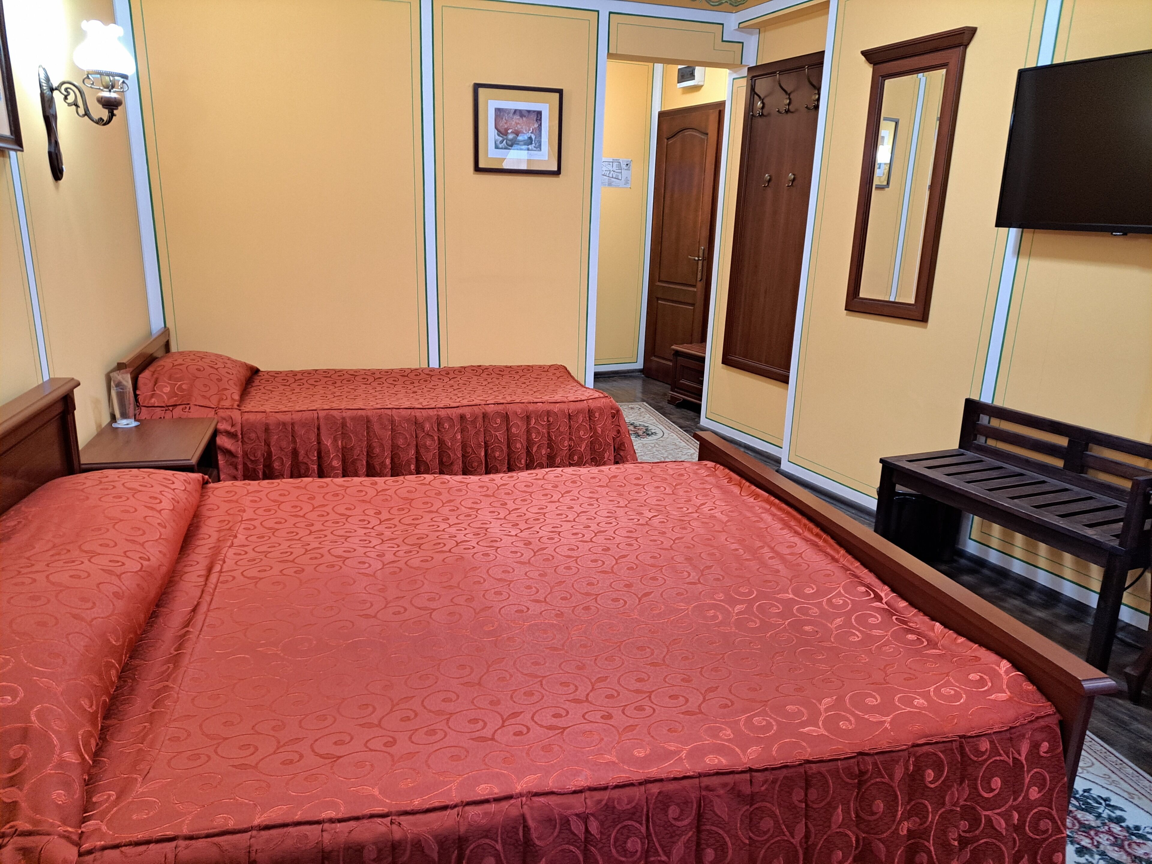 Habitación de hotel con dos camas, un banco, un televisor y una puerta que da a otra habitación.