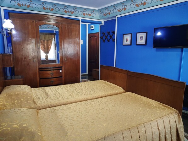 A hotel room with a bed, a wardrobe, a mirror, a television, and a wall with framed pictures.