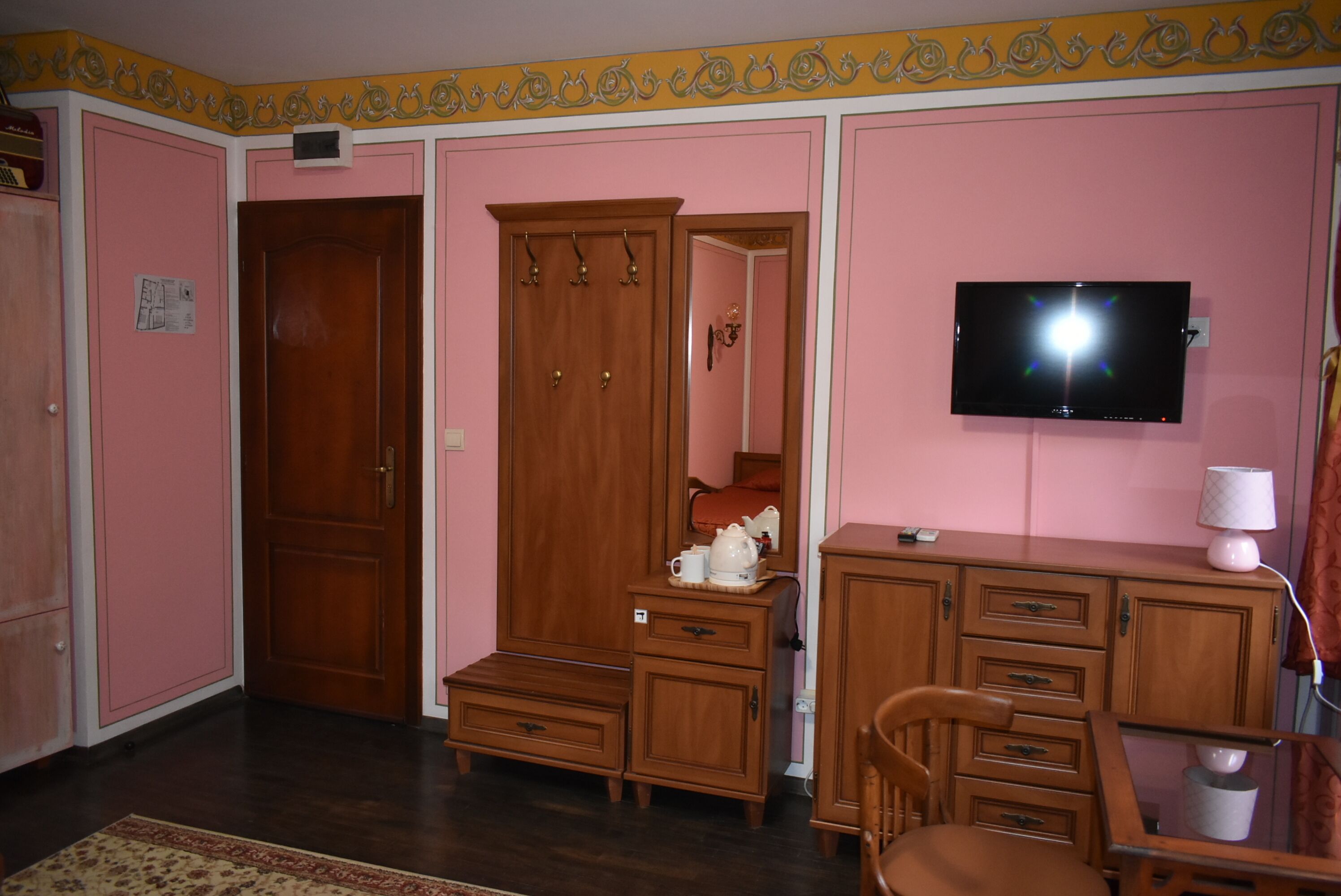 A room with pink walls, a wooden wardrobe, a television, and a desk with drawers.