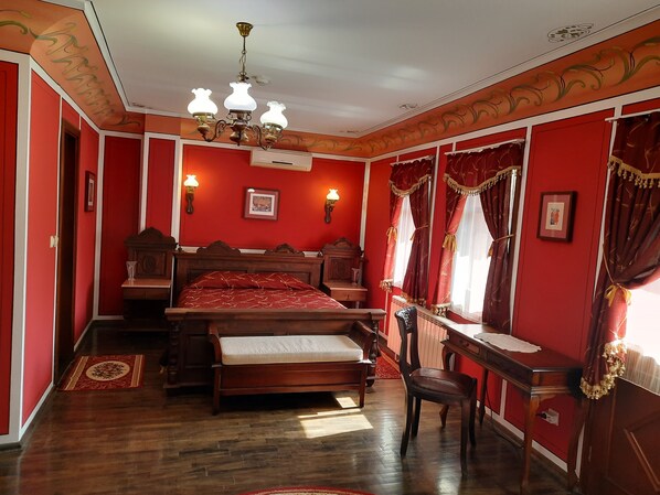 A bedroom with a wooden bed, a desk, and a chair. There are two wall-mounted lamps and a chandelier.