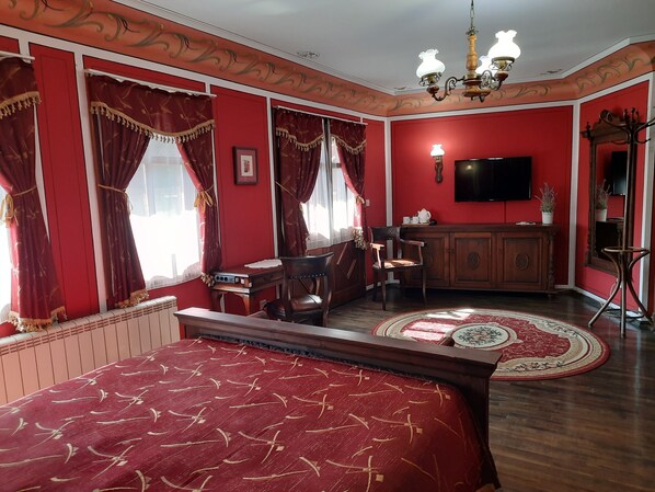 A room with a large bed, a desk, a chair, a television, and a cabinet.