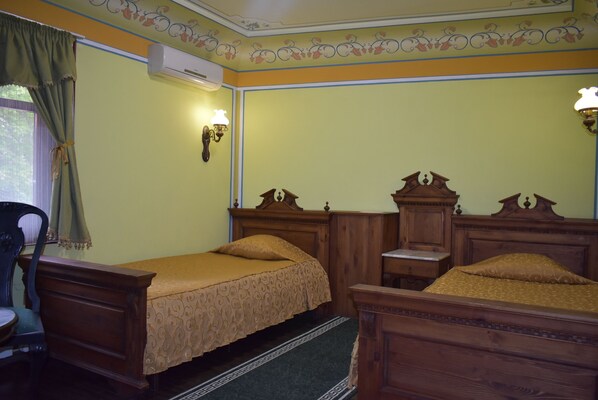 A room with two wooden beds, a chair, a small table, and an air conditioning unit.