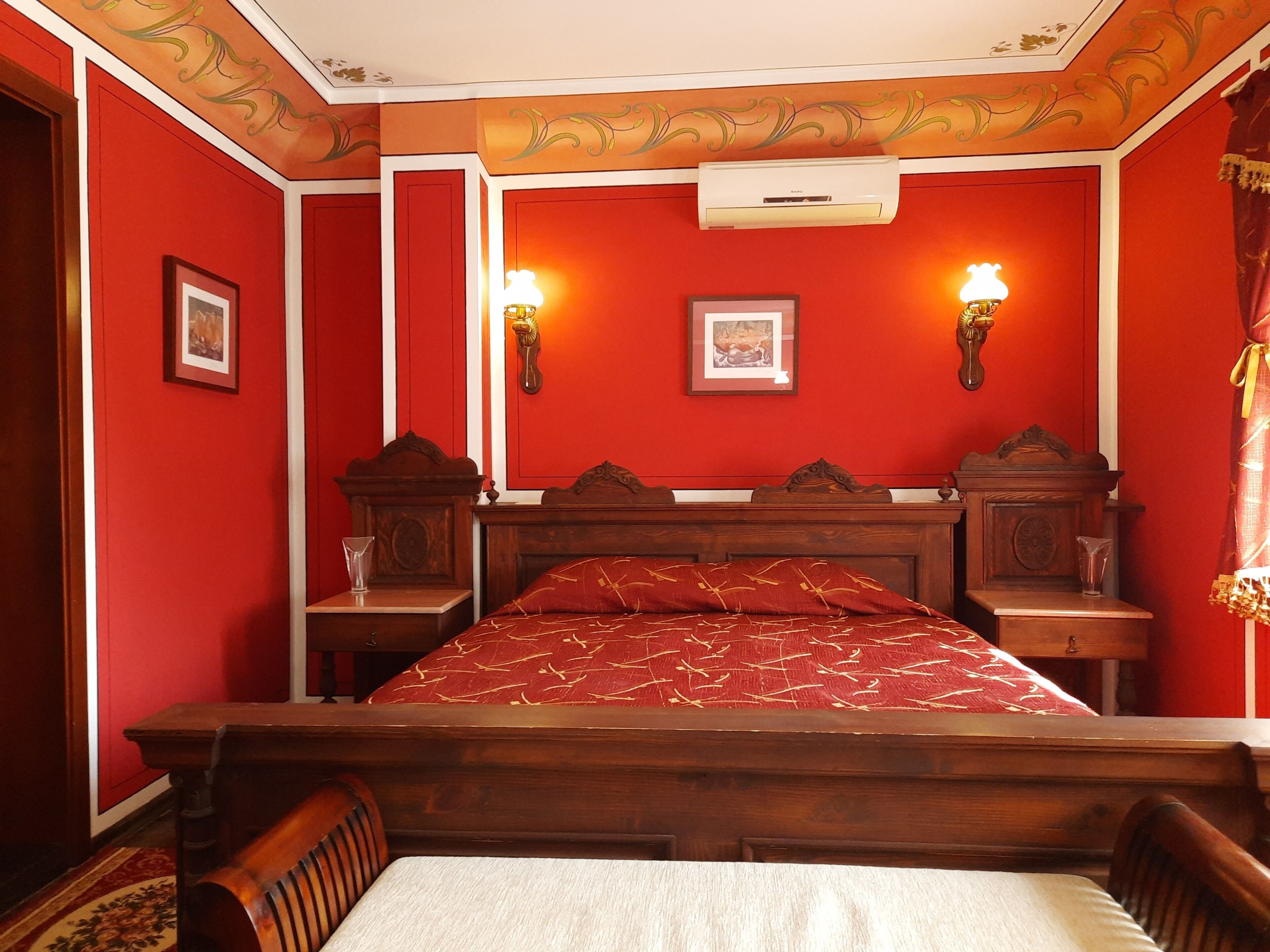 Une chambre avec un lit en bois, des murs rouges et deux lampes fixées au mur.