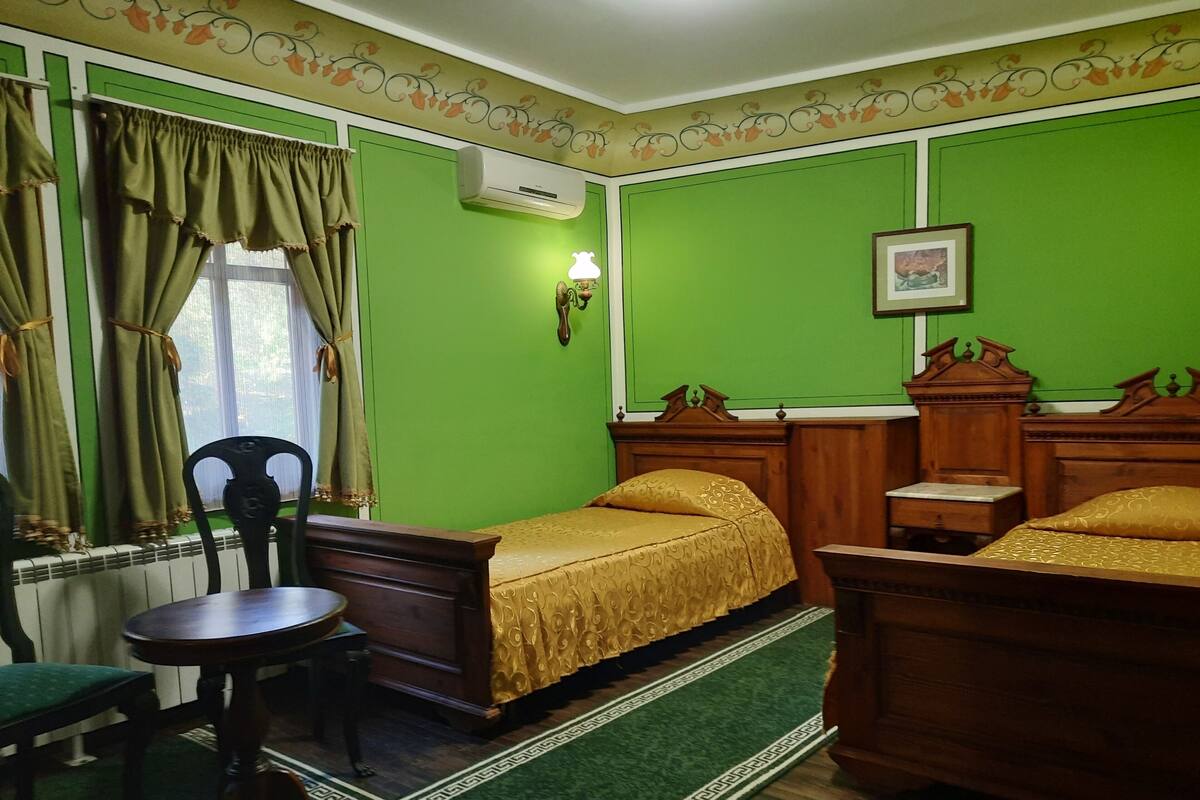 Une pièce avec deux lits en bois, une petite table ronde, une chaise, un radiateur et une fenêtre avec des rideaux.