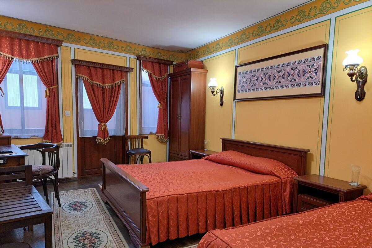 Une chambre d’hôtel avec deux lits, un bureau, une chaise et une fenêtre avec des rideaux.
