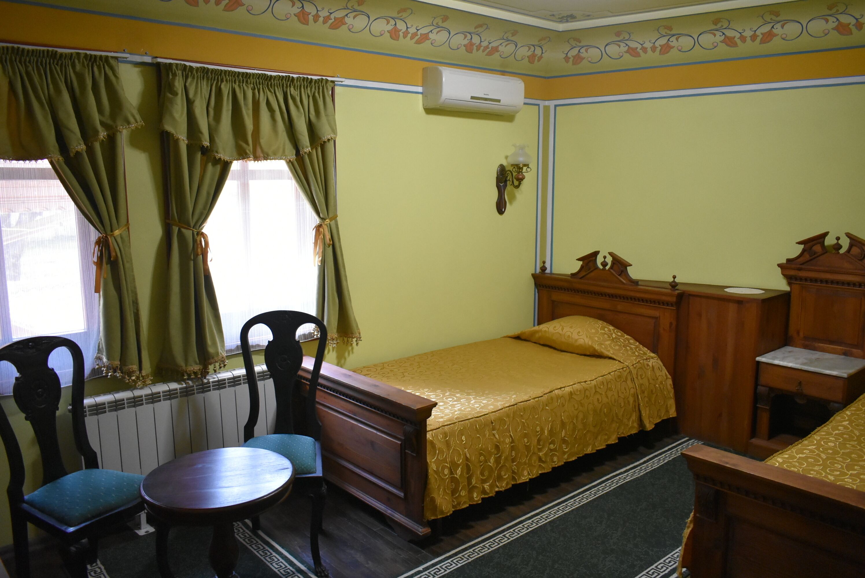 A room with a bed, a wooden dresser, a chair, a small table, and a radiator.