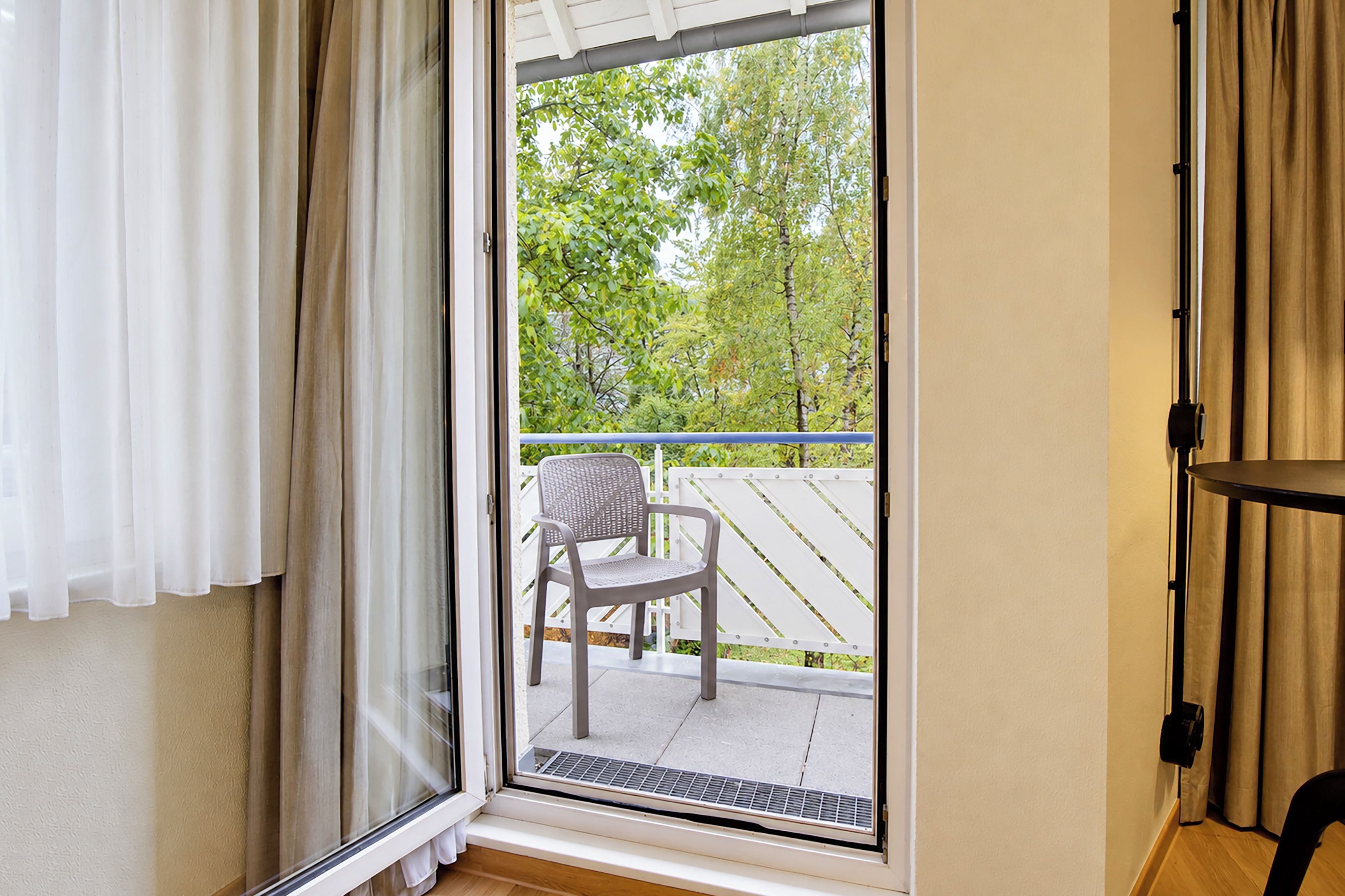 A room with a sliding glass door leading to an outdoor area with a chair and a white fence.