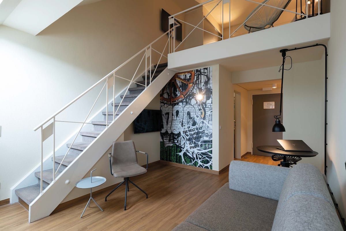 A modern interior with a staircase, a wall mural, a laptop on a table, and a sofa.