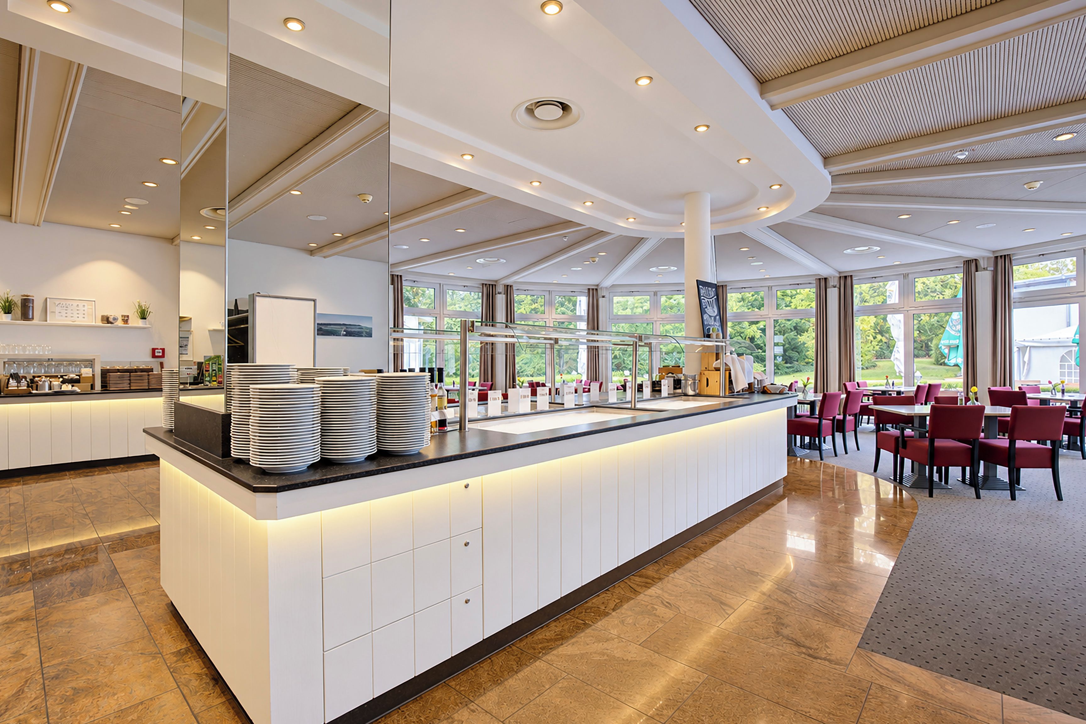 A modern hotel lobby with a central reception desk, seating area, and large windows offering a view of the outdoors.