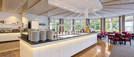 A modern hotel lobby with a central reception desk, seating area, and large windows offering a view of the outdoors.