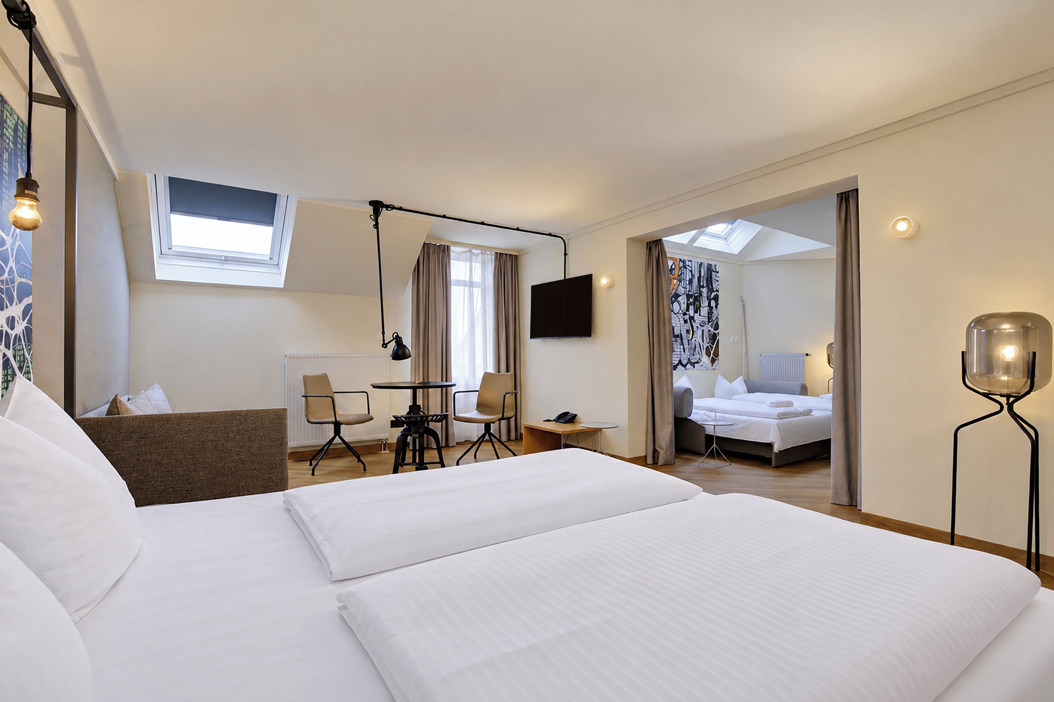 A hotel room with a large bed, a desk with two chairs, a TV, and a bathroom visible through an open door.