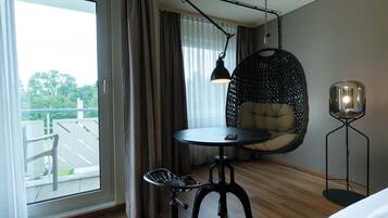 Moderni hotellihuone, jossa on suuri ikkuna, pyöreä pöytä, riipputuoli ja lattiavalaisin.