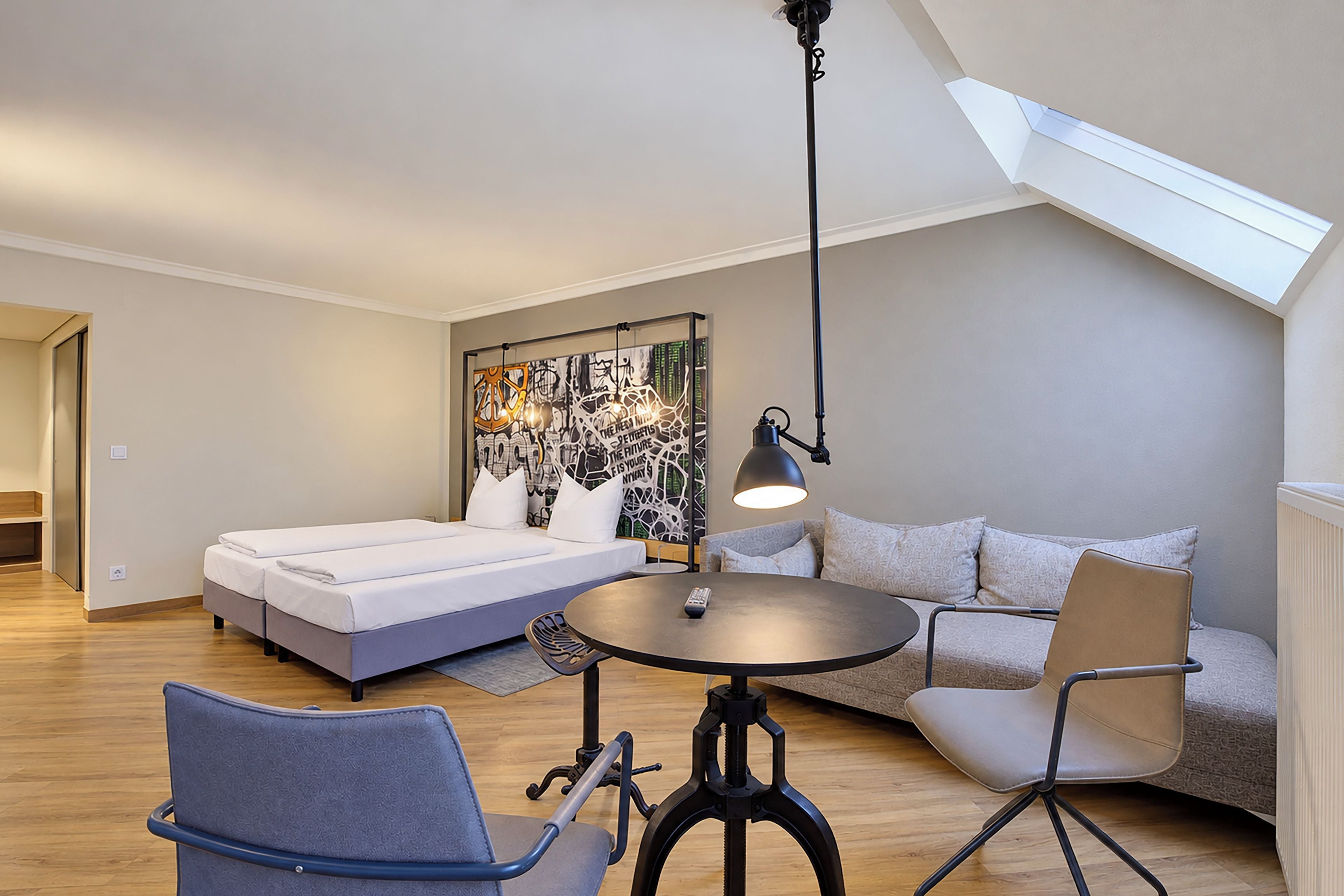 A modern, well-lit room with a bed, a sofa, a dining table, and a ceiling skylight.
