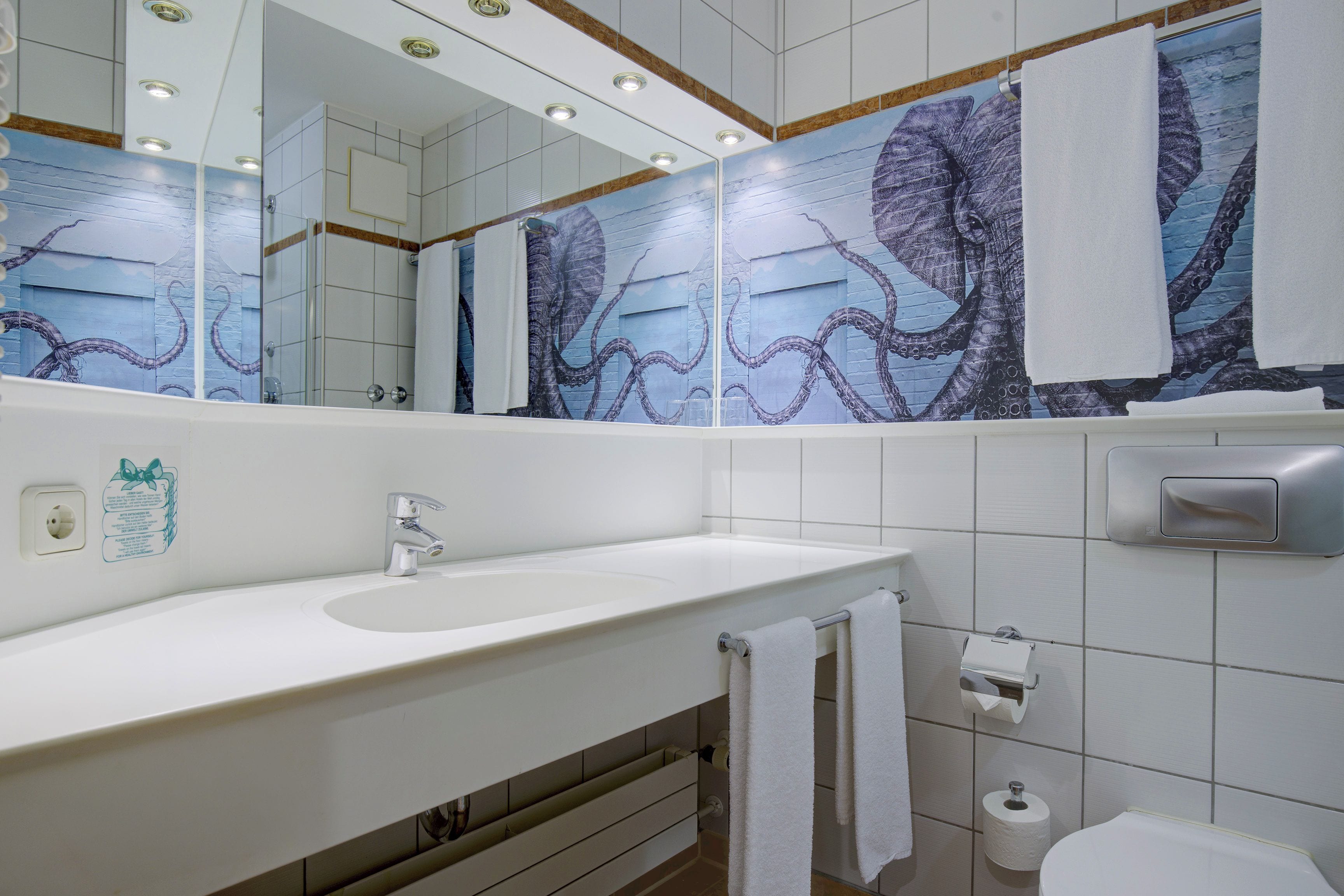 Une salle de bain avec un lavabo blanc, un miroir, un porte-serviettes et des toilettes.