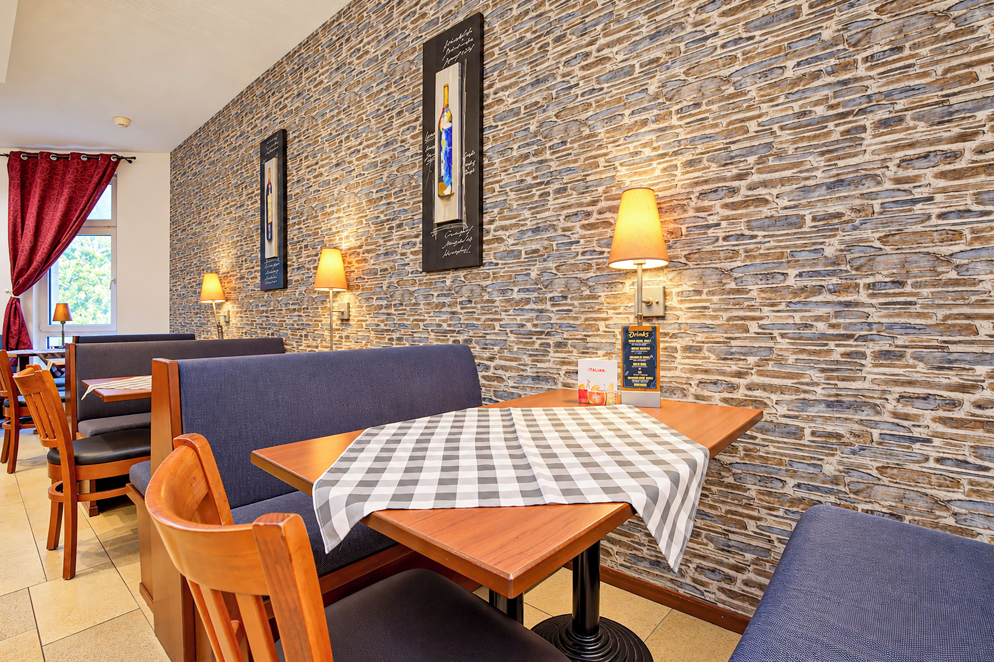 L’intérieur d’un restaurant avec des murs en pierre, des tables en bois et des sièges recouverts d’un tissu bleu.