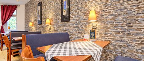 L’intérieur d’un restaurant avec des murs en pierre, des tables en bois et des sièges recouverts d’un tissu bleu.
