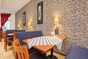 Een restaurantinterieur met stenen muren, houten tafels en blauwe bekleding.