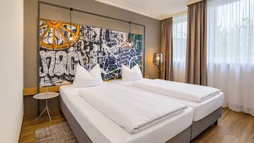 A hotel room with two beds, a large abstract painting on the wall, a small side table, and a window with curtains.
