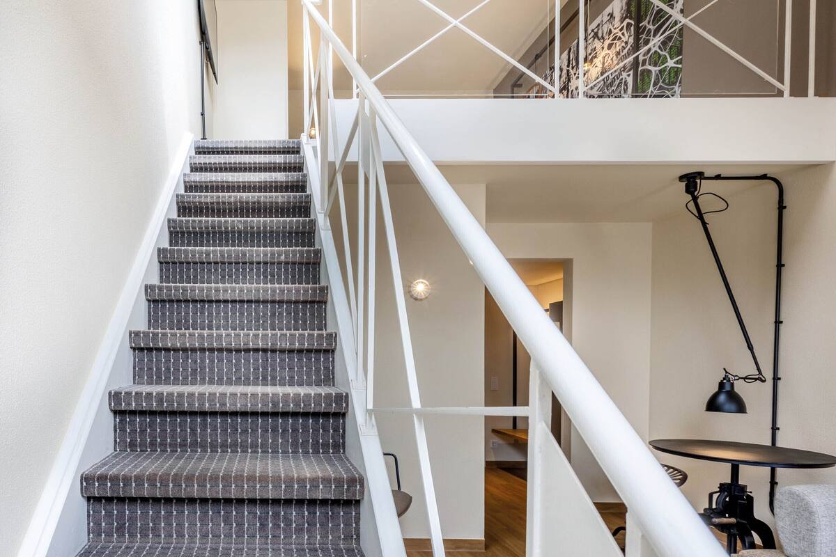A staircase with a checkered carpet, white railings, and a black desk lamp.