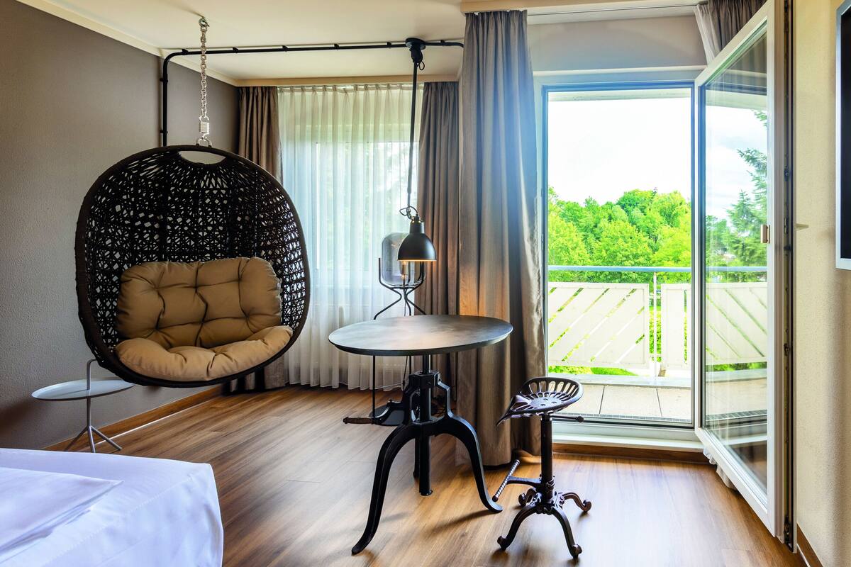 A modern room with a hanging chair, a small round table, and a view of a balcony.