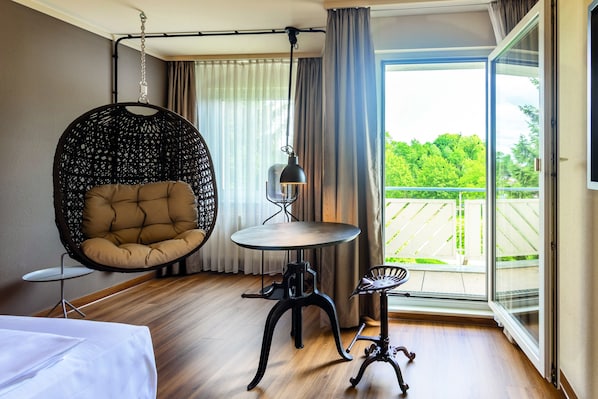 Una habitación moderna con una silla colgante, una mesita redonda y vistas a un balcón.