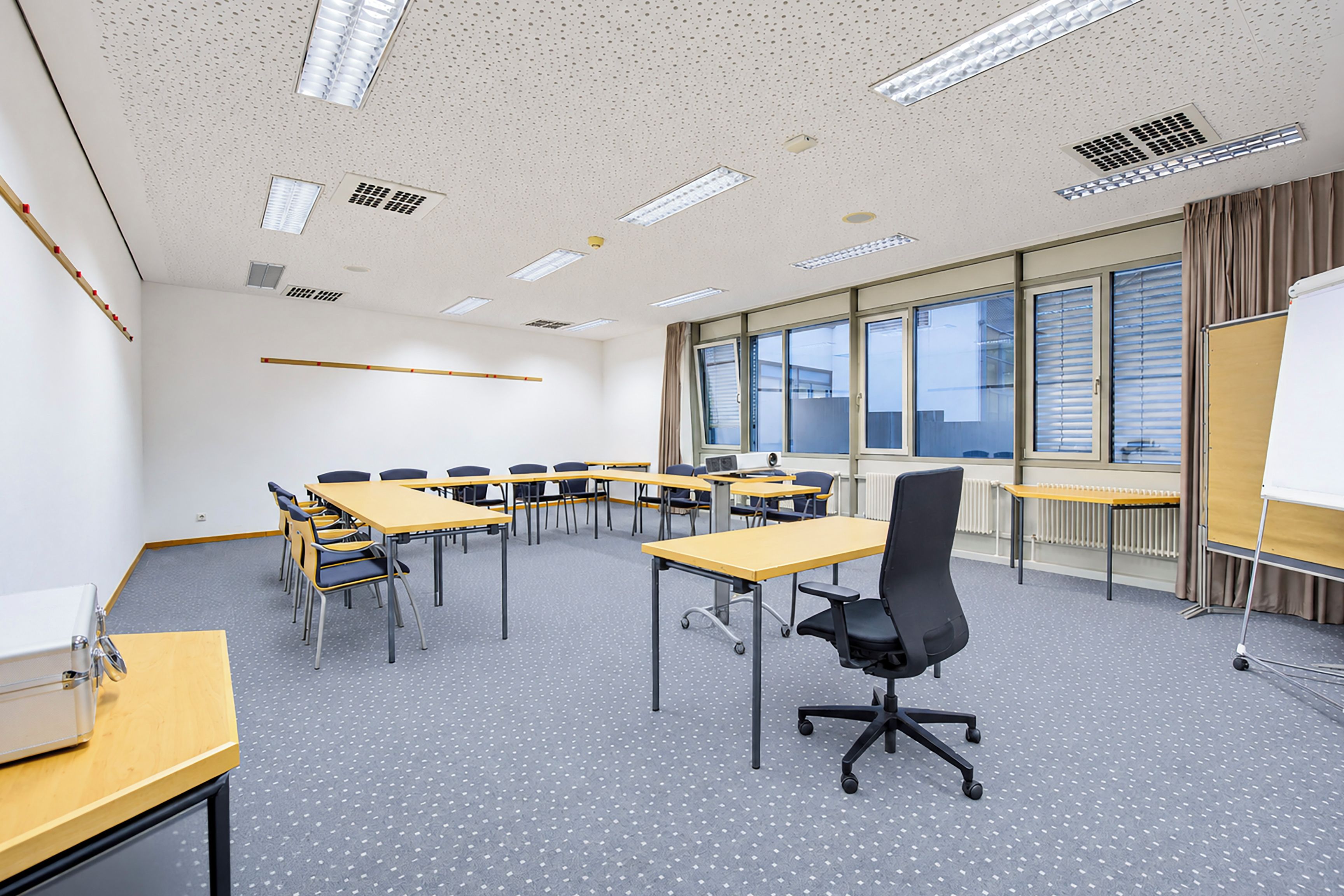 Ein Konferenzraum mit Tischen, Stühlen, einer Whiteboard-Tafel und großen Fenstern.