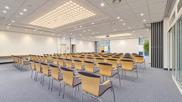 Une salle de conférence avec des rangées de chaises, un écran de projection et une grande fenêtre.