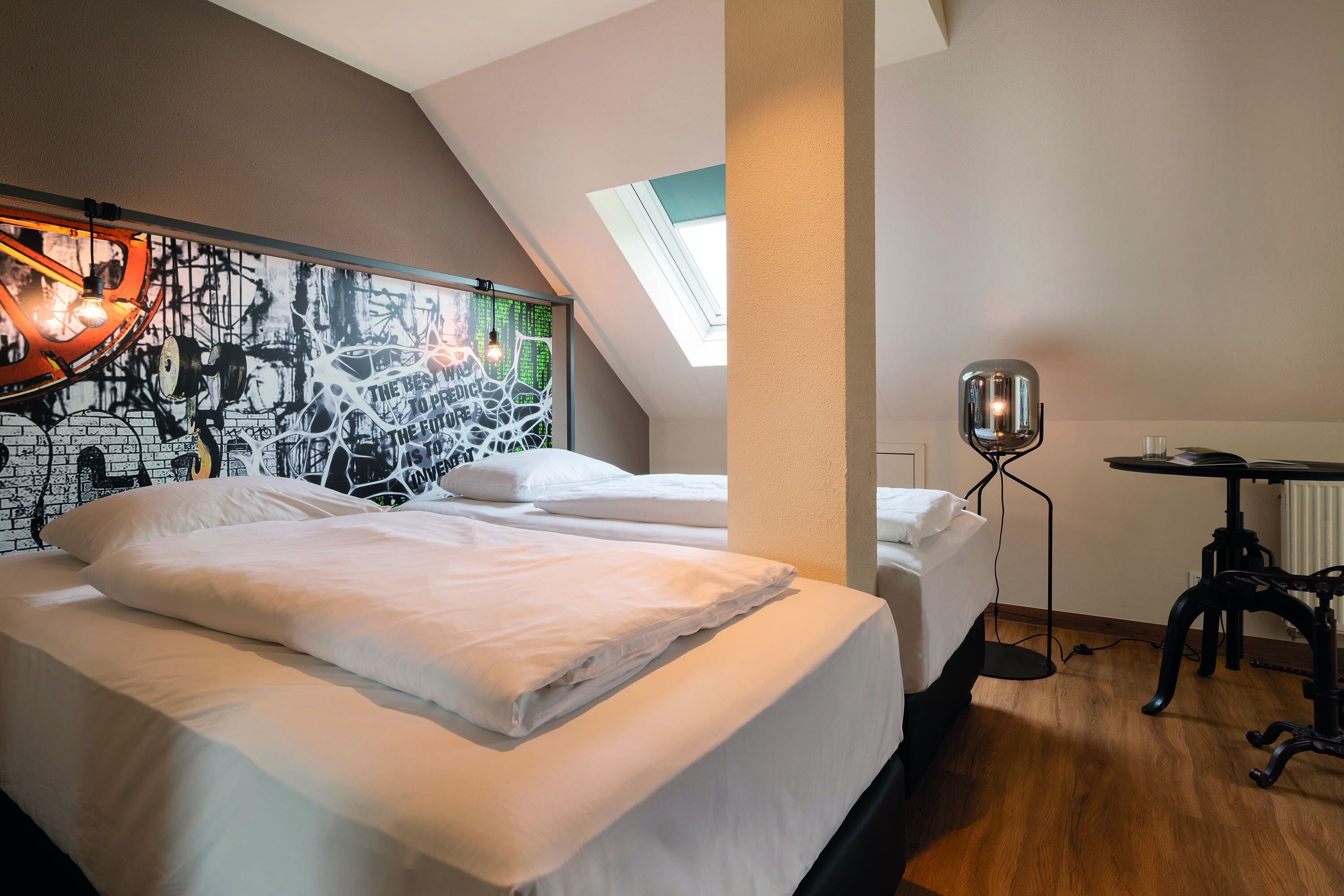 Habitación de hotel moderna con dos camas, un tragaluz, un escritorio y un mural único en la pared.