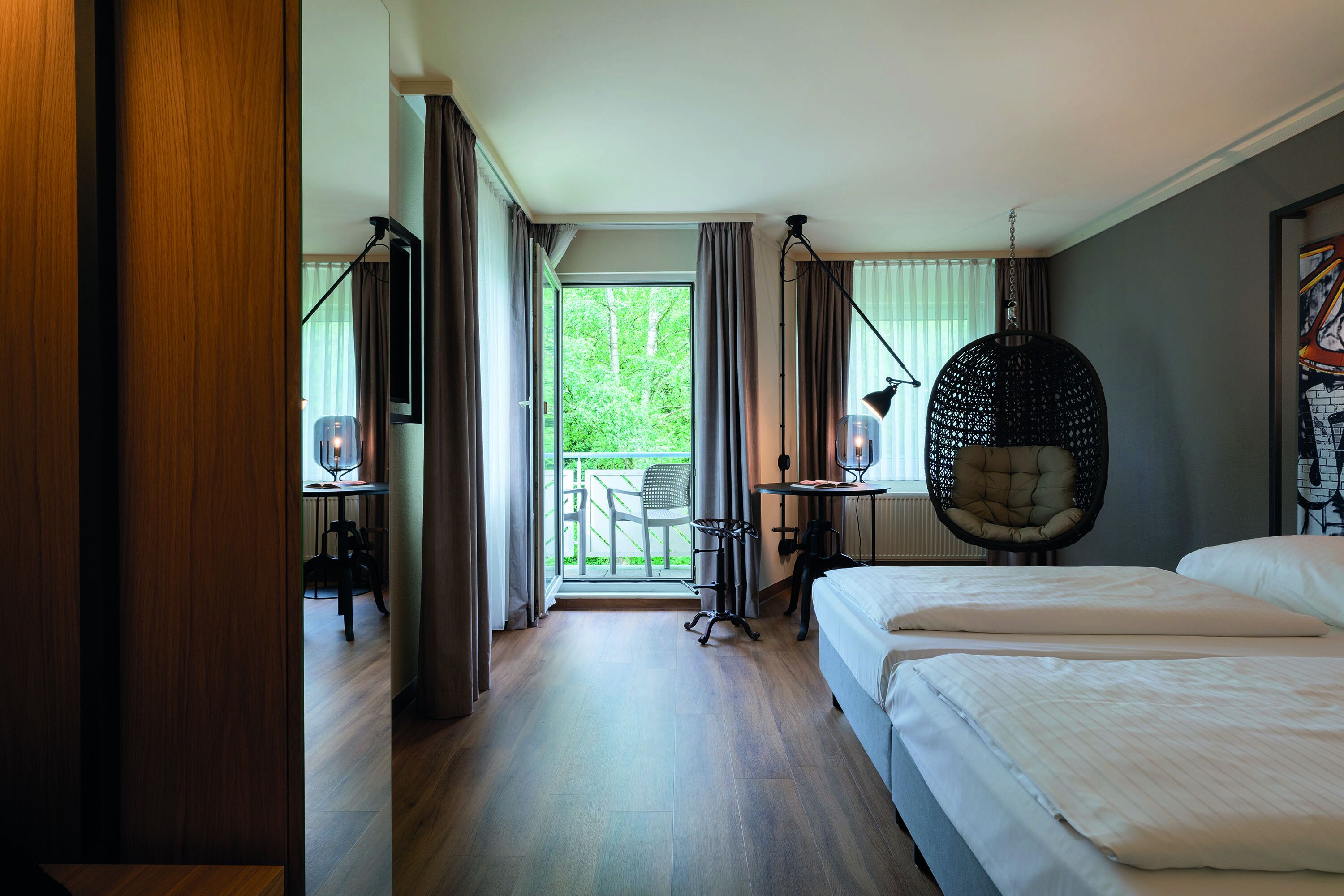 A hotel room with two beds, a balcony with a chair, and a hanging chair.