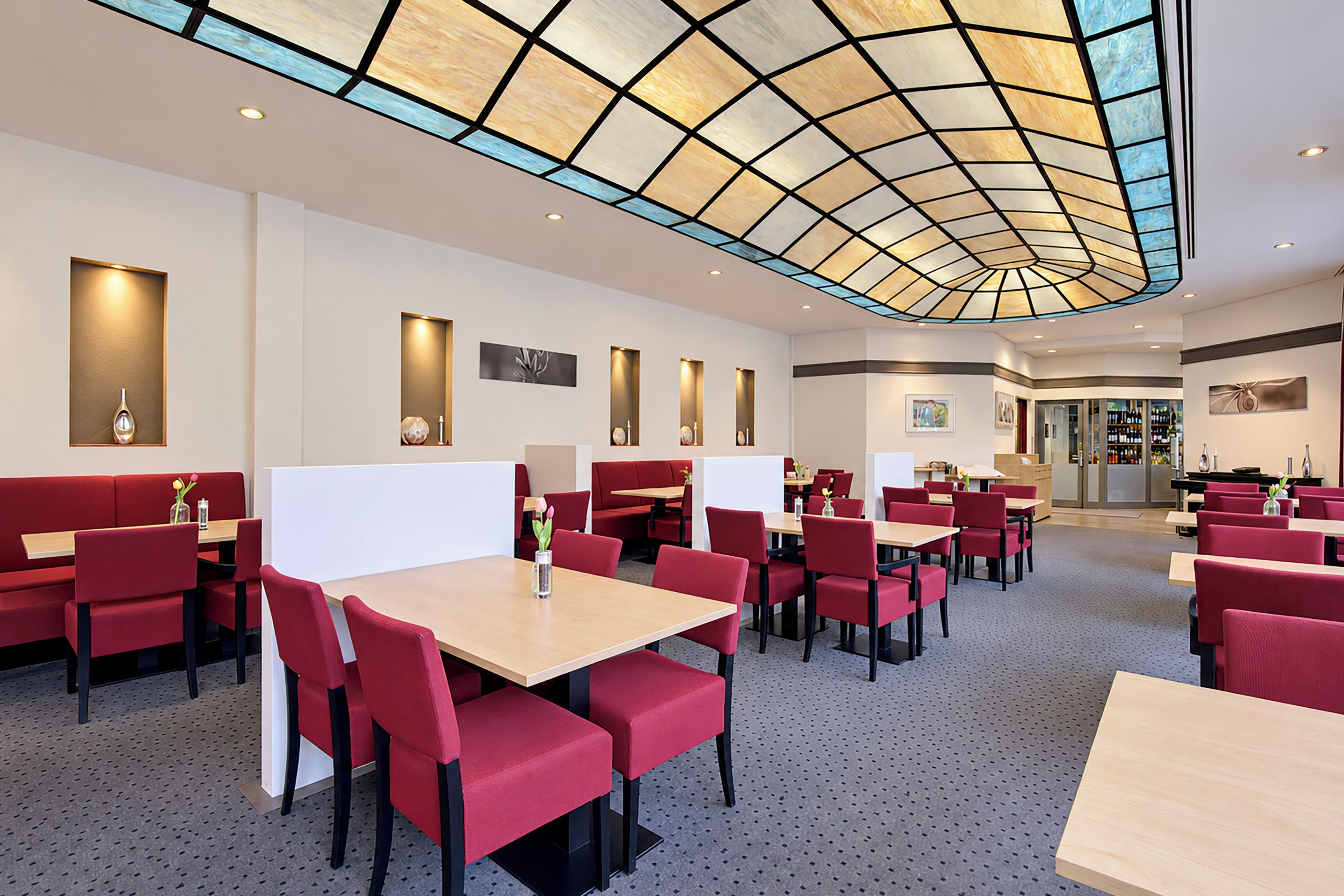 Un restaurante con cabinas y mesas, techo con diseño y zona de bar.