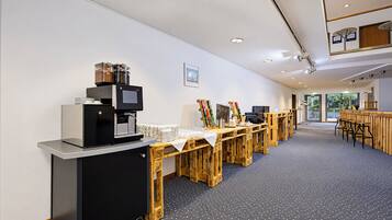 Moderni hotellin aula, jossa on kahvipiste, puupöytiä ja näkymä ulos.
