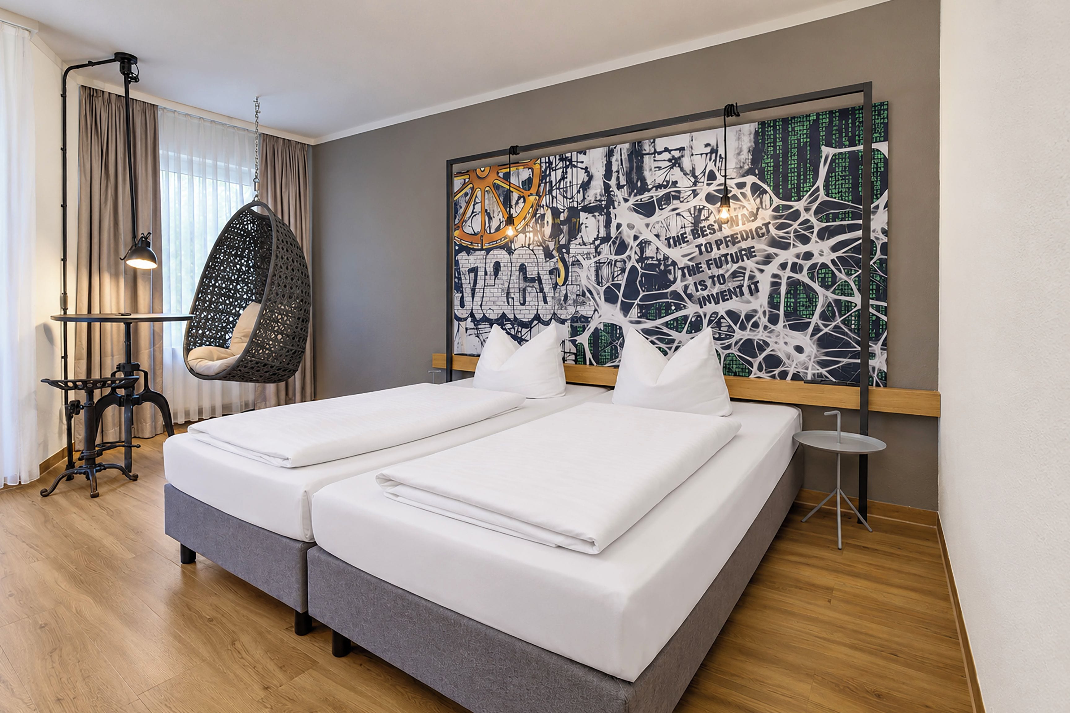A hotel room with a double bed, a hanging chair, a large abstract painting, and a small table.