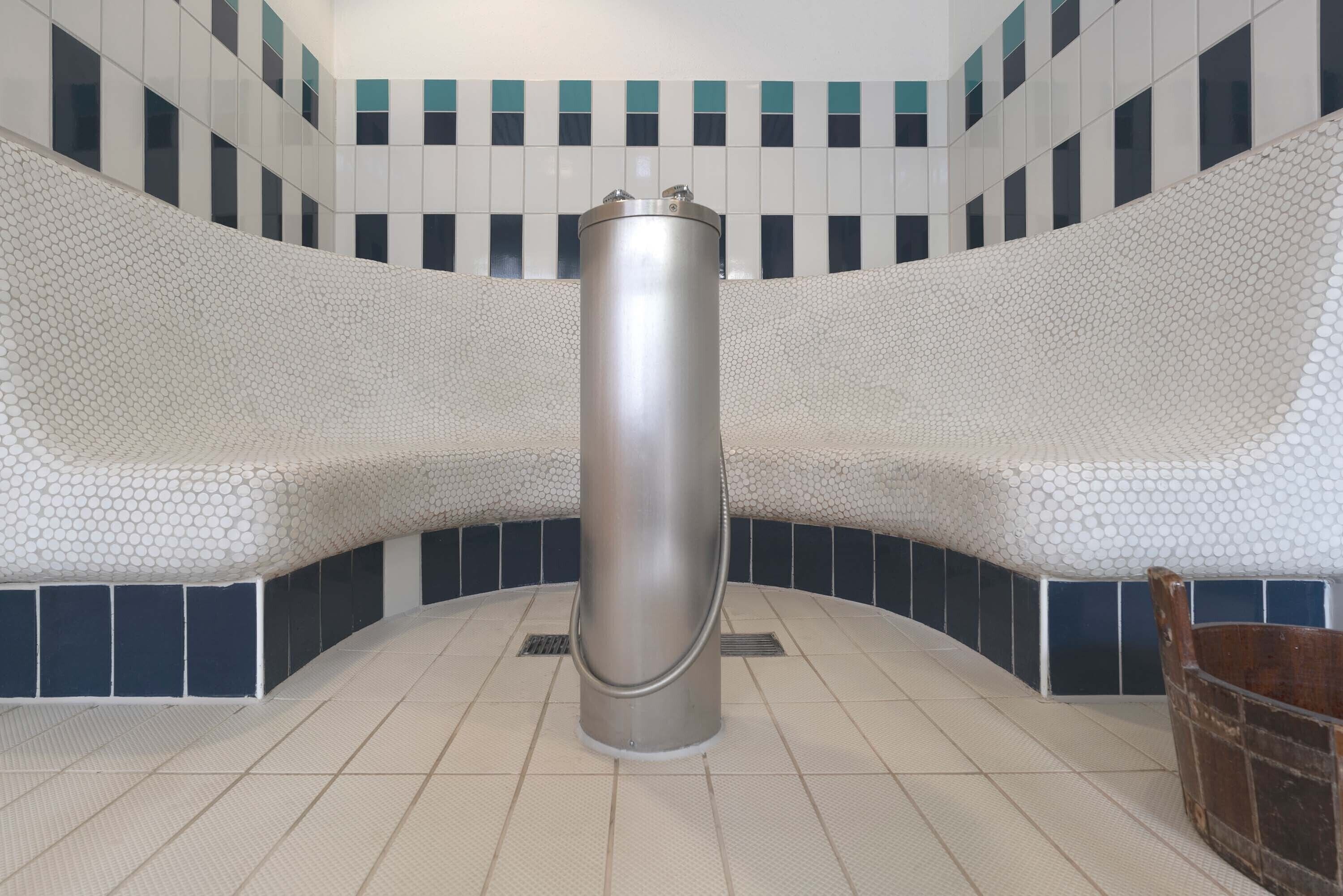 A modern bathroom with a central cylindrical object, possibly a water feature, surrounded by a tiled wall with a geometric pattern.