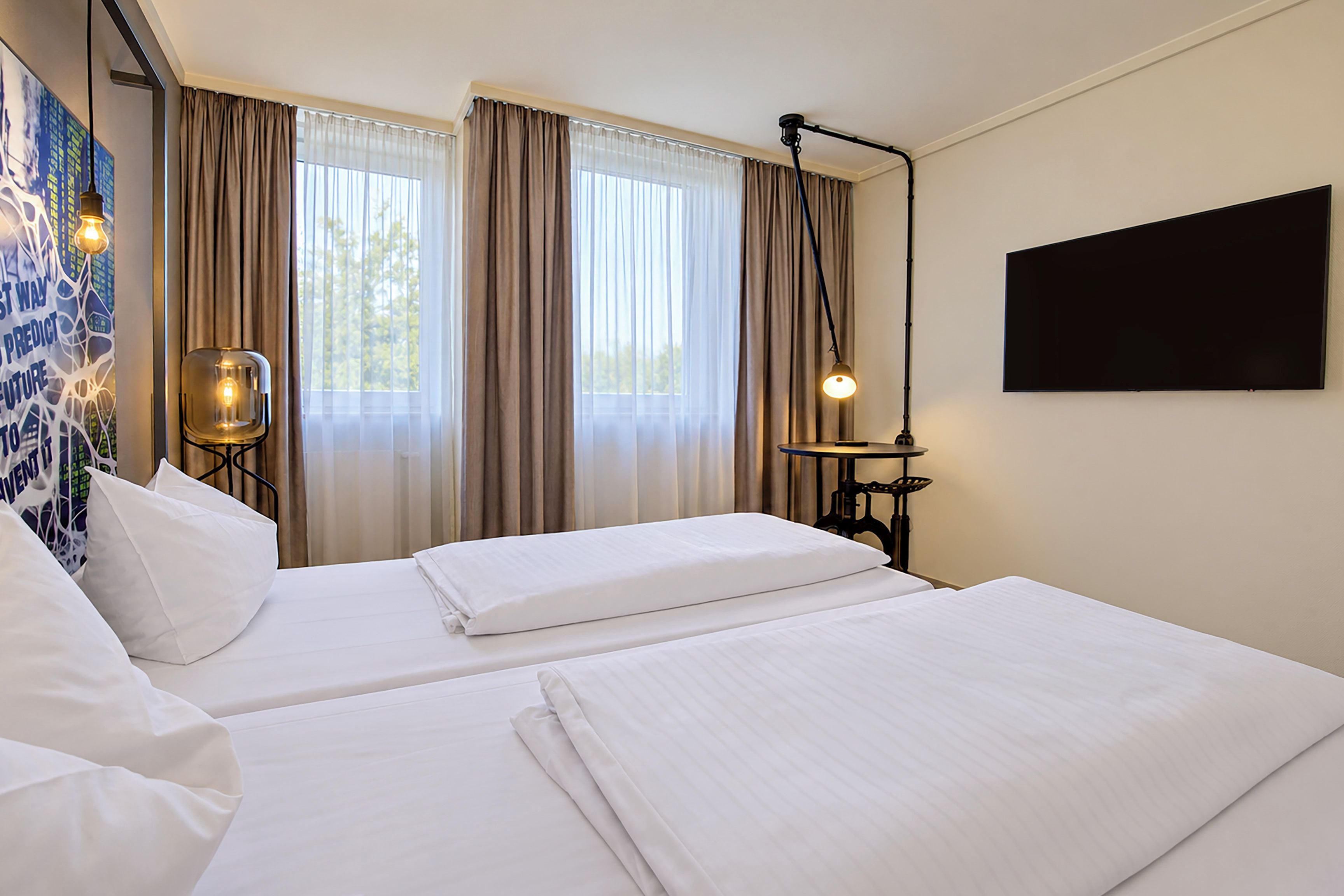 Ein Hotelzimmer mit zwei Betten, einem großen Fenster mit Vorhängen, einem an der Wand montierten Fernseher und einer dekorativen Leuchte.