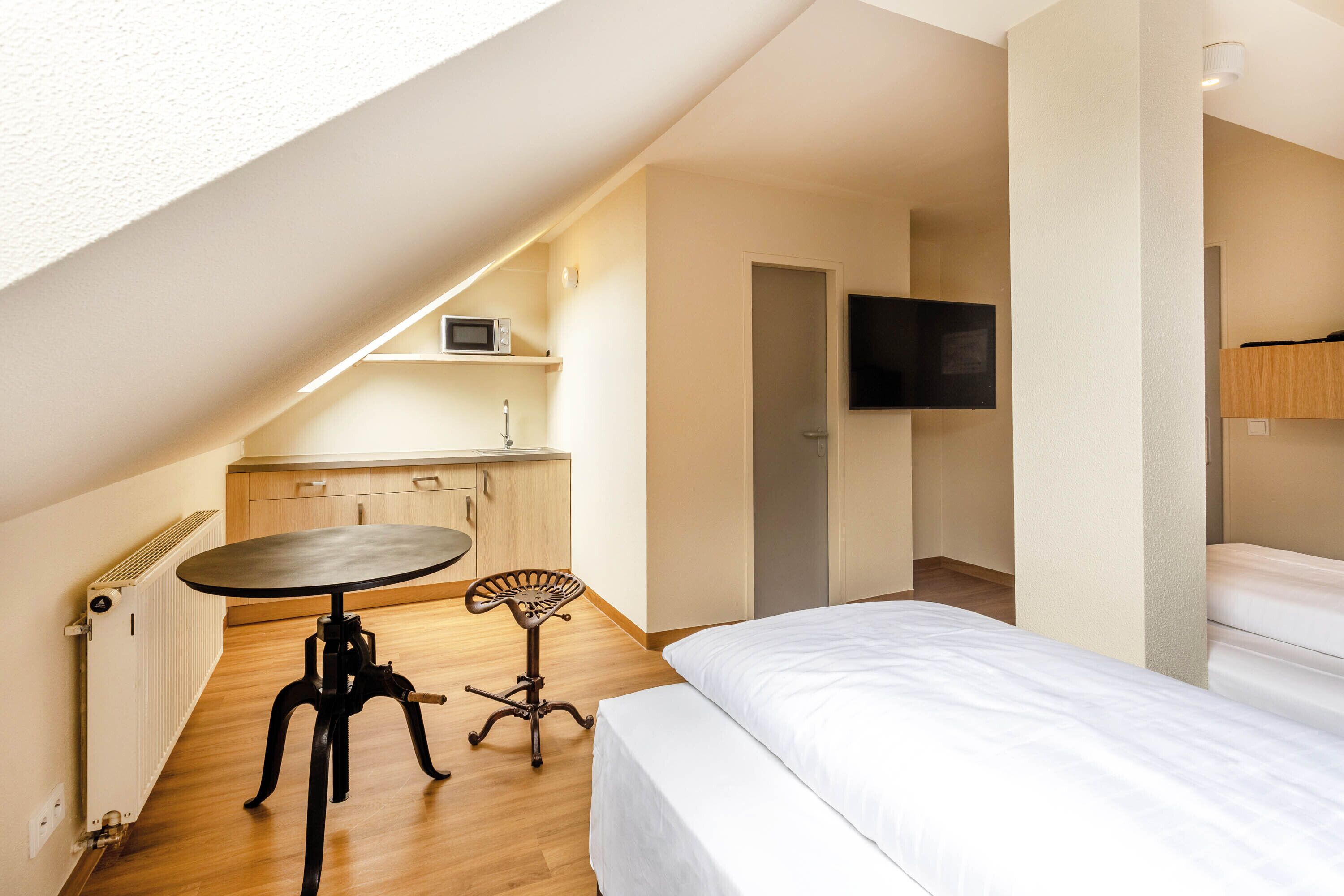 A compact room with a bed, a small table, a chair, a microwave, and a TV.