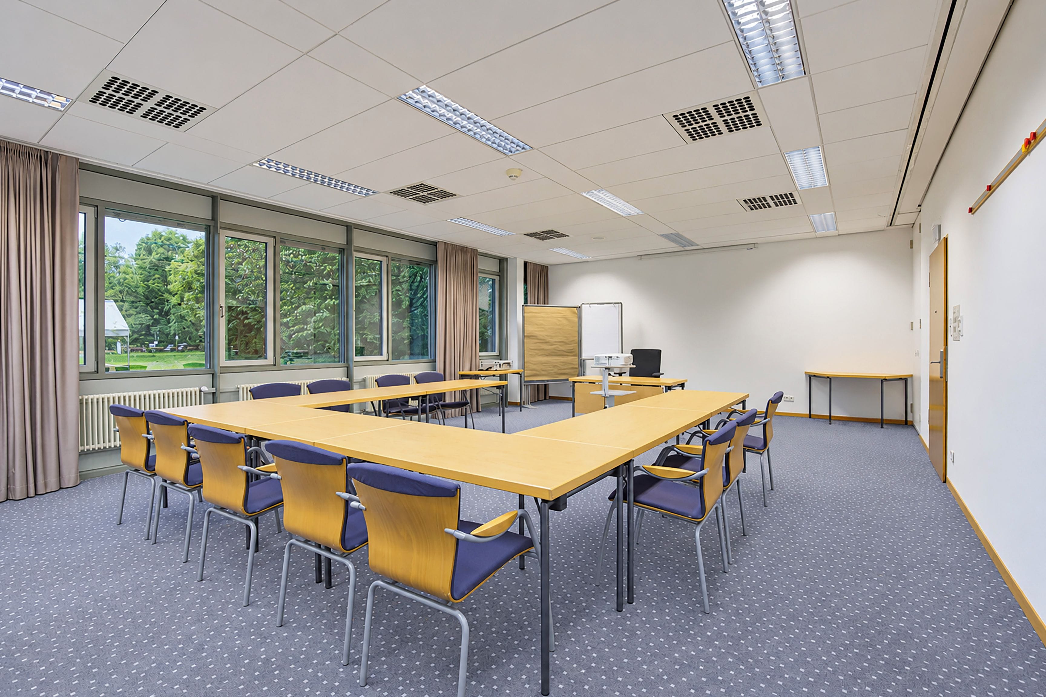 Ein Konferenzraum mit einem langen Tisch, Stühlen, einer Tafel und großen Fenstern.