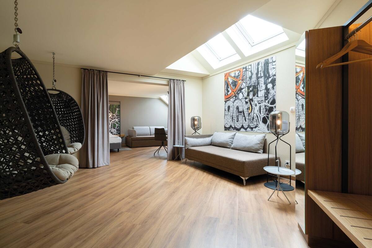 A spacious living room with a hanging chair, a sofa, a small table, and a large window with a skylight.