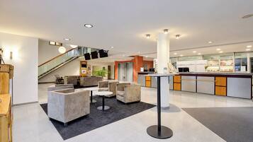 A modern lobby with a reception desk, seating area, and a staircase.